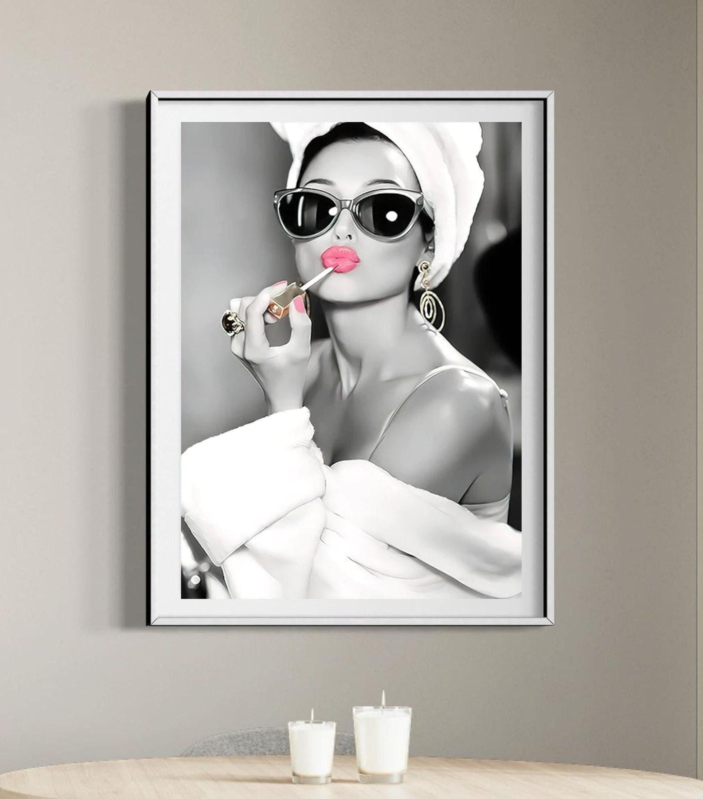 This elegant black-and-white portrait features Audrey Hepburn in a white robe and towel, wearing oversized sunglasses and gold earrings. Her lips and nails are highlighted in bold pink as she applies lipstick, adding a striking pop of colour. The vintage-inspired artwork exudes sophistication and luxury, capturing Hepburn’s timeless Hollywood glamour. A chic, fashion-forward print perfect for modern interiors and fans of iconic beauty.