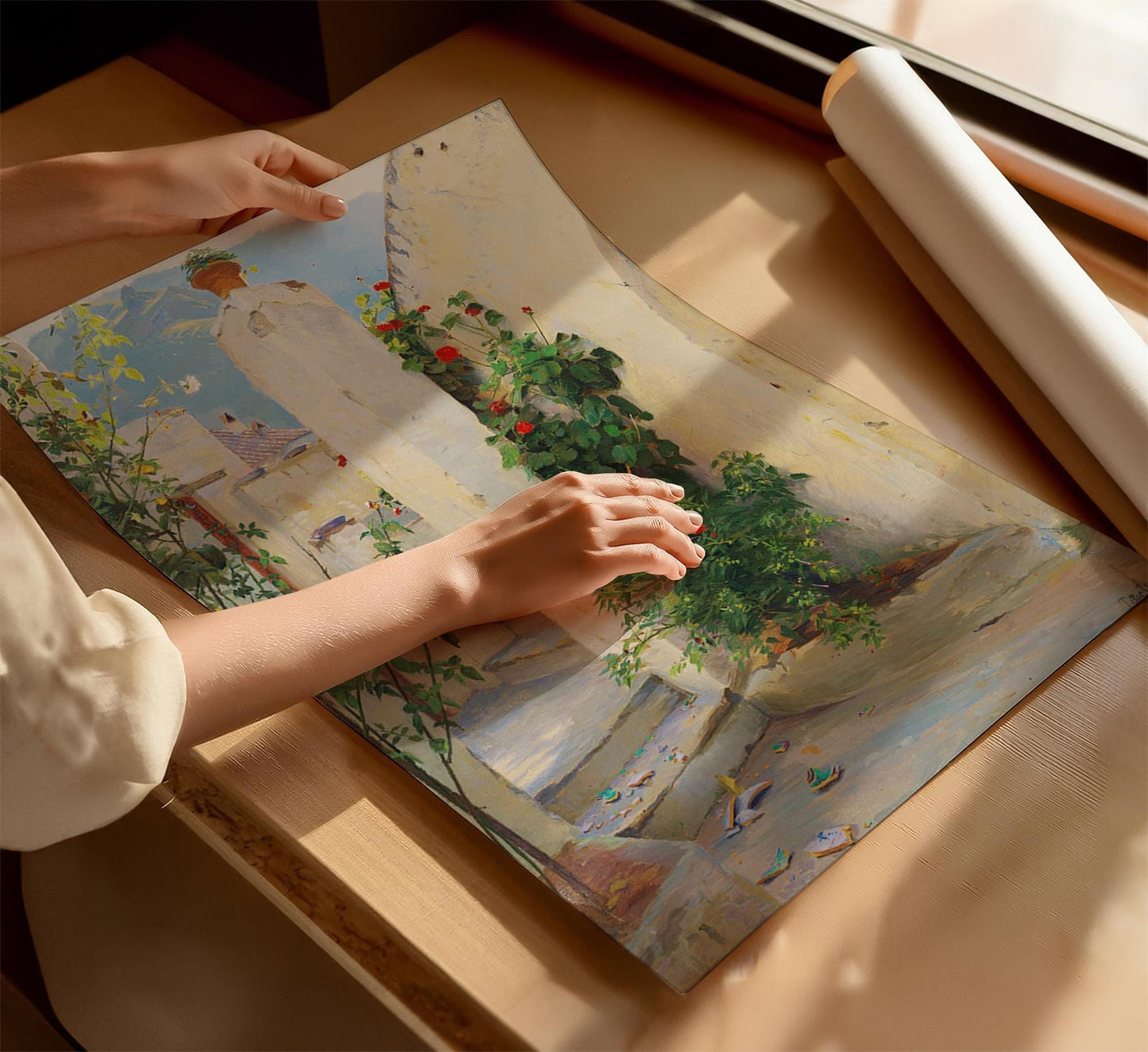A person's hands are holding a framed painting of a garden scene, with a white paper roll visible in the background.