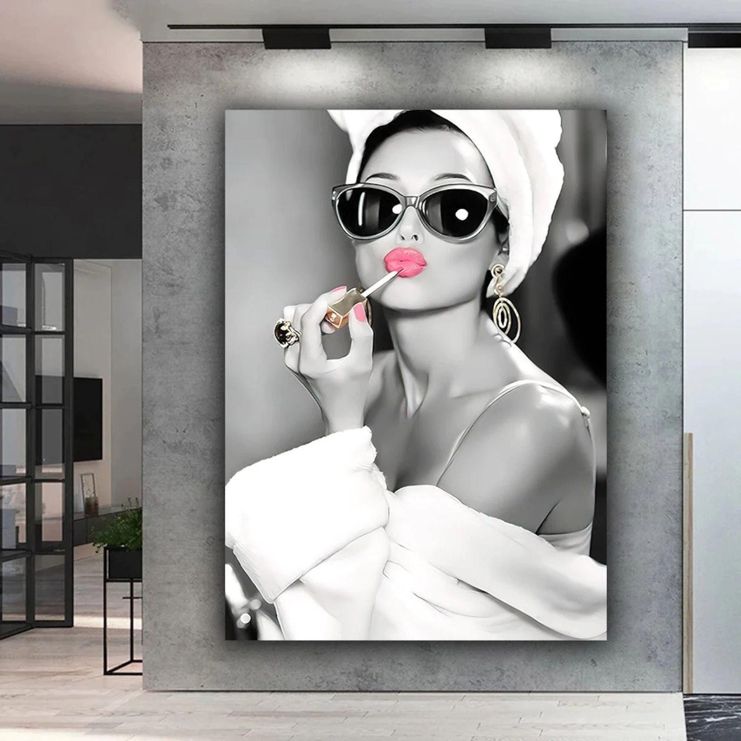 This elegant black-and-white portrait features Audrey Hepburn in a white robe and towel, wearing oversized sunglasses and gold earrings. Her lips and nails are highlighted in bold pink as she applies lipstick, adding a striking pop of colour. The vintage-inspired artwork exudes sophistication and luxury, capturing Hepburn’s timeless Hollywood glamour. A chic, fashion-forward print perfect for modern interiors and fans of iconic beauty.